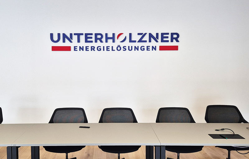 Individuelles lackiertes 3D Wandlogo von Unterholzner Energielösungen an einer weißen Innenwand im Besprechungsraum.jpg